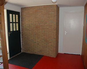 Ruime entree van vakantiehuis Krekel, Nes, Ameland met houten trap, biedt een warm welkom op de Waddeneilanden.