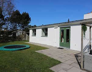 Zijaanzicht van bungalow Patrijs in Nes, Ameland, met trampoline en groene tuin op de Waddeneilanden.
