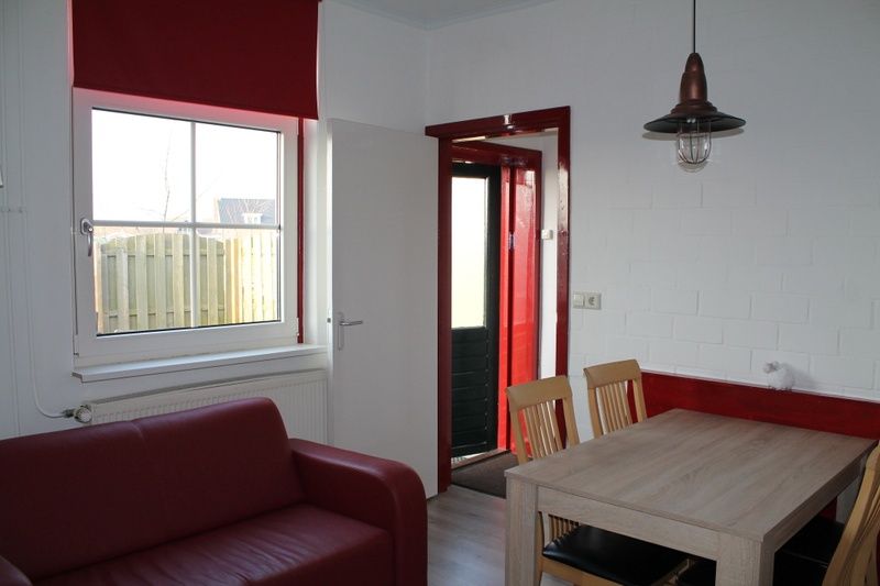 Knusse woonkamer van Onder de vuurtoren 115, Texel, met rode bank en eettafel, ideaal voor een ontspannen verblijf.