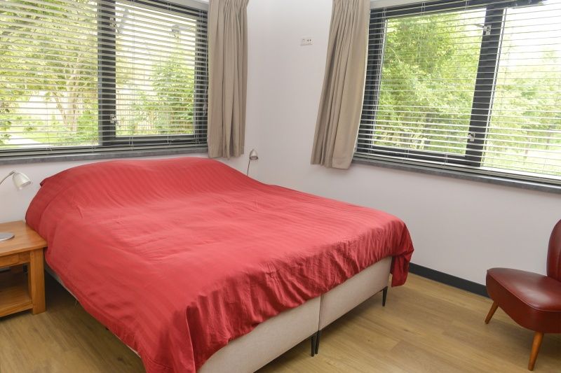 Slaapkamer met groot raam in De Postschipper vakantiehuis in De Cocksdorp, Texel, met uitzicht op de tuin.