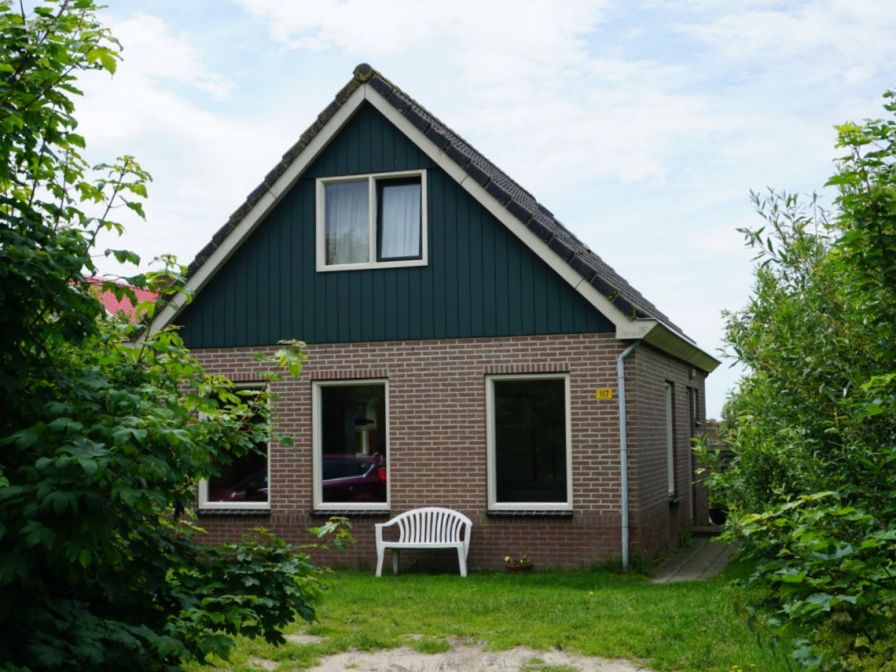 Dune/lighthouse view detached vacation home in De Cocksdorp, Texel with green garden and bench in front.