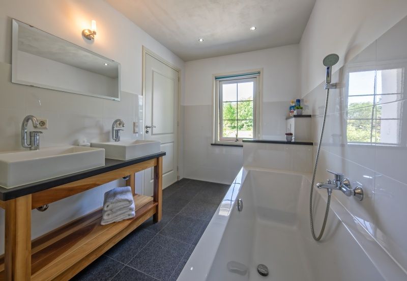 Moderne badkamer met bad en dubbele wastafel in Vakantiehuis Paal 86, Texel.