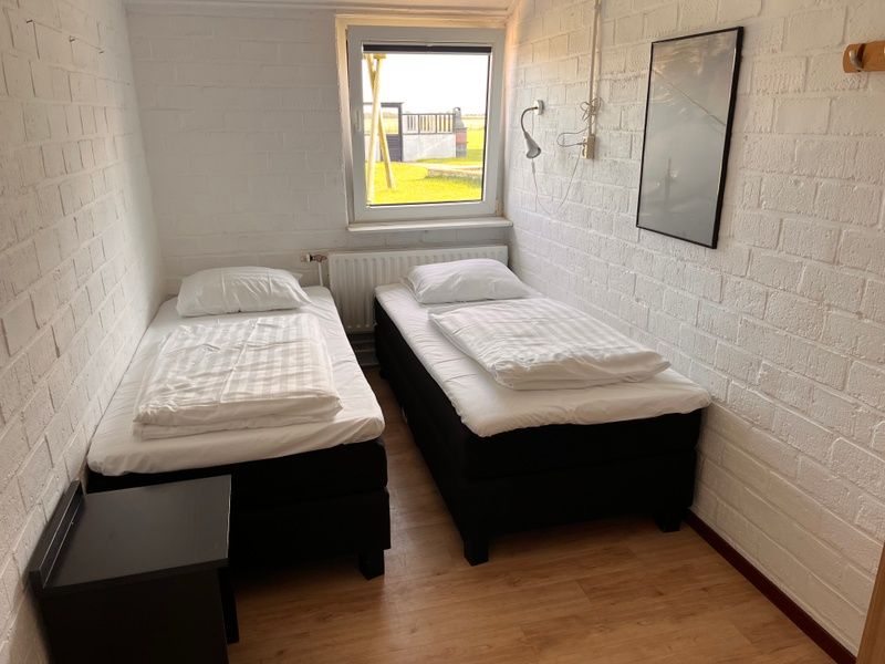 Slaapkamer in Noorderwind vakantiehuis, De Cocksdorp, Texel met twee comfortabele bedden en uitzicht op de tuin.