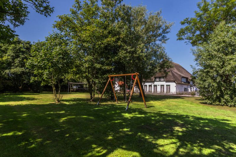 Speelruimte met schommel bij Type R vakantiewoning, De Cocksdorp, Texel, omgeven door groene bomen.