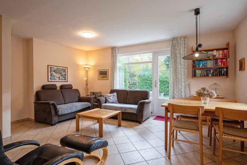 Cozy living room of Holiday home Slufterduin 094 in De Cocksdorp, Texel, with comfortable seating area and views of the green garden.