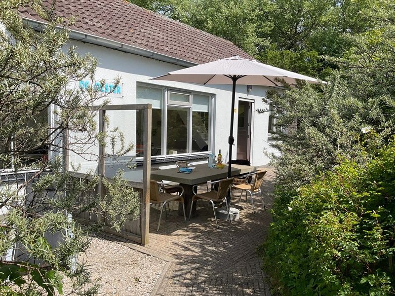 Terras met parasol bij Bungalow Schelpenoord - Vakantiehuis De Oester, De Cocksdorp, Texel, omgeven door groen.
