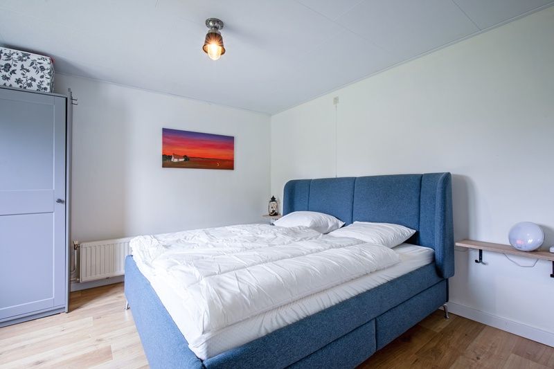 Comfortabele slaapkamer in vakantiehuis Muyweg 062, De Cocksdorp, Texel met groot bed en kunst aan de muur.