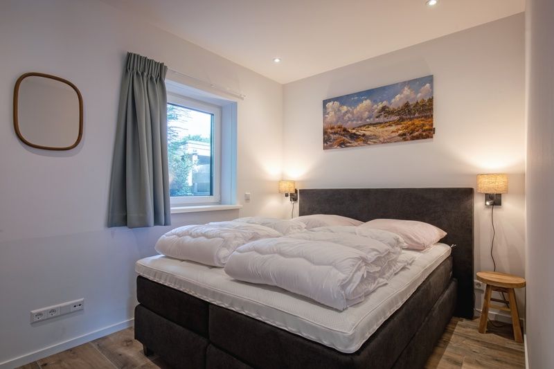 Comfortabele slaapkamer in Vakantiehuis Slufterhoek 104, De Cocksdorp, Texel met groot bed en sfeervolle verlichting.