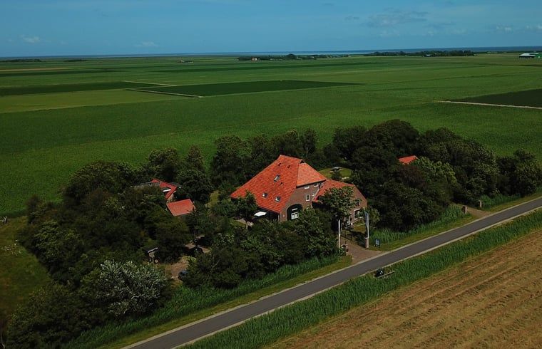 Luchtfoto van Vakantiehuisje in De Cocksdorp, Texel, omgeven door weelderige natuur en groene velden op de Waddeneilanden.