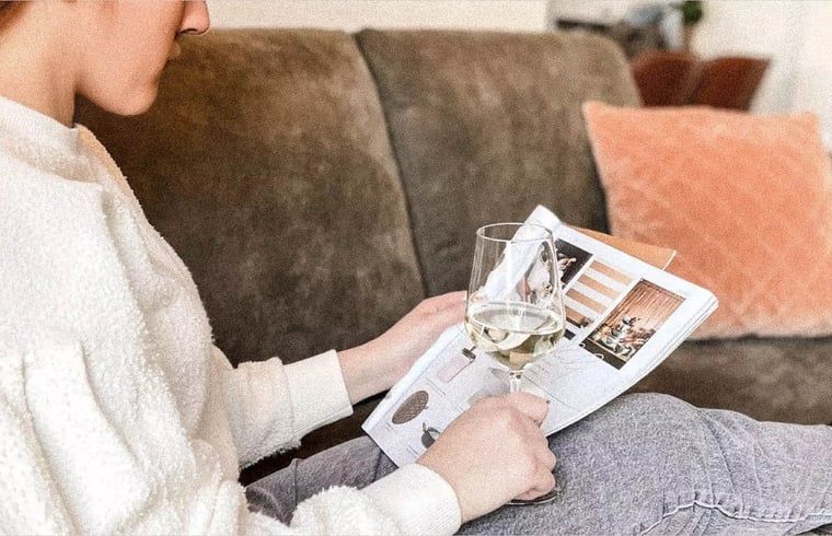 Ontspanning in Vakantiehuisje in De Cocksdorp, Texel met een glas wijn en tijdschrift, genietend van het comfort op de Waddeneilanden.