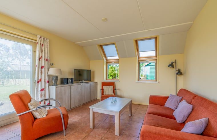 Lichte woonkamer in Vakantiehuisje in De Cocksdorp, Texel met comfortabele zithoek en uitzicht op de tuin, ideaal voor ontspanning.