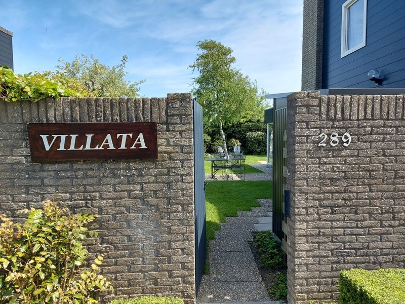 Ingang van Vakantiehuis B 289 in De Cocksdorp, Texel, omgeven door een groene tuin en rustieke stenen muren.