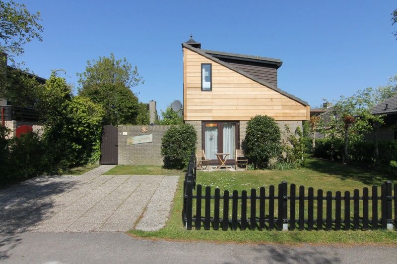 Vacation home A 167 in De Cocksdorp, Texel, surrounded by green garden and wooden veranda, ideal for a relaxing stay on the Wadden Islands.