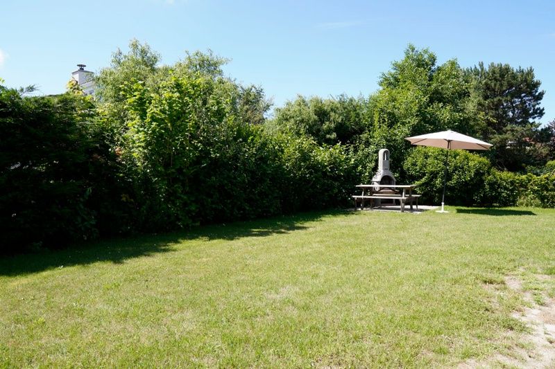 Spacious garden at Holiday home D 669 in De Cocksdorp, Texel with green surroundings and terrace with parasol, ideal for relaxation on the Wadden Islands.
