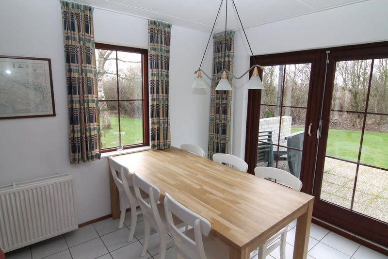 Cozy dining room in Holiday home D 745, De Cocksdorp, Texel overlooking green garden and spacious wooden table.