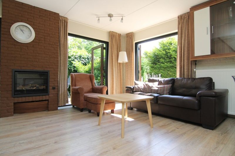 Gezellige woonkamer in Vakantiehuis A 383, De Cocksdorp, Texel. Comfortabele zithoek met uitzicht op groene tuin, ideaal voor ontspanning.