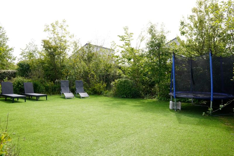 Geraeumiger Garten im Ferienhaus D 439 in De Cocksdorp, Texel, mit Liegestuehlen und Trampolin, umgeben von gruener Natur.