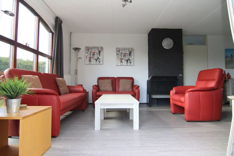 Gezellige woonkamer in Vakantiehuis E 407, De Cocksdorp, Texel, met comfortabele rode banken en moderne inrichting.