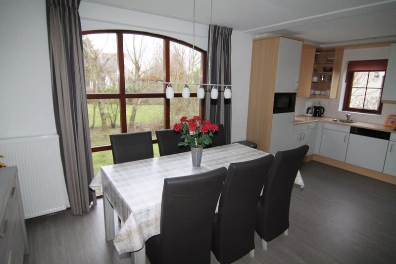 Gezellige eetkamer in Vakantiehuis E 407, De Cocksdorp, Texel met uitzicht op tuin en moderne keuken, ideaal voor familievakanties op de Waddeneilanden.