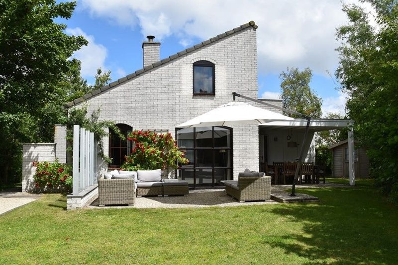 Vakantiehuis F 455 in De Cocksdorp, Texel biedt een charmant terras met comfortabele zithoek en parasol, omgeven door groene natuur.