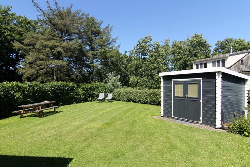 Spacious garden of Holiday Home F 776 in De Cocksdorp, Texel, with green lawn and wooden shed, ideal for relaxation on the Wadden Islands.