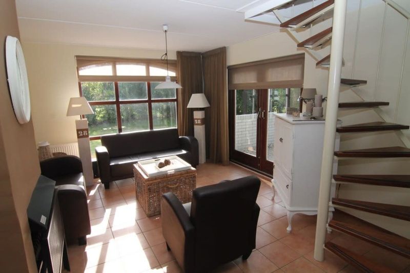 Gemuetliches Wohnzimmer im Ferienhaus F 713 in De Cocksdorp, Texel mit komfortabler Sitzecke und Blick auf die gruene Umgebung.