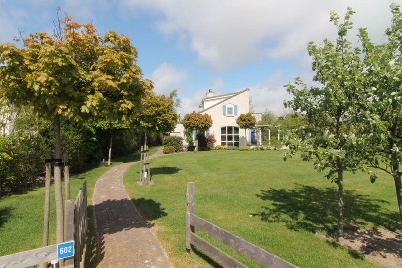 Vakantiehuis F 602 in De Cocksdorp, Texel, omgeven door weelderig groen en een uitnodigend pad naar de voordeur op de Waddeneilanden.