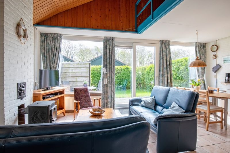 Gezellige woonkamer van Vakantiehuis Slufterhoek 110 in De Cocksdorp, Texel met uitzicht op groene tuin en comfortabele zithoek.