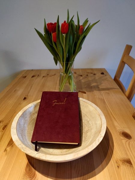 Detail des Esstisches im Ferienhaus Kikkerpoel, De Cocksdorp, Texel mit Tulpen und einem Tagebuch.