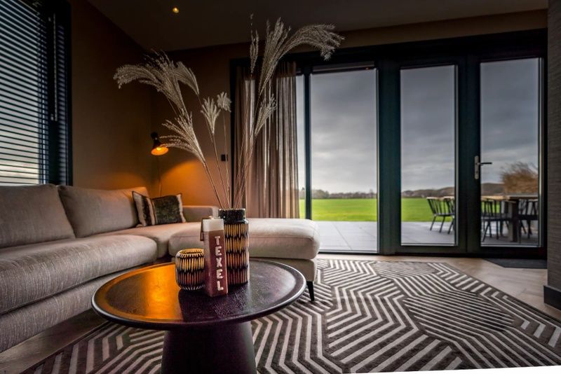 Uitzicht vanuit de woonkamer van 6 persoons vakantiewoning in De Cocksdorp, Texel met groot raam naar terras.