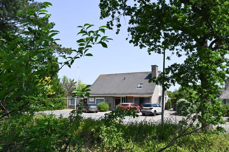 Vooraanzicht van Tesselhuus met zorgvleugel, vakantiehuis in De Koog, Texel, met parkeerplaats en groene omgeving.