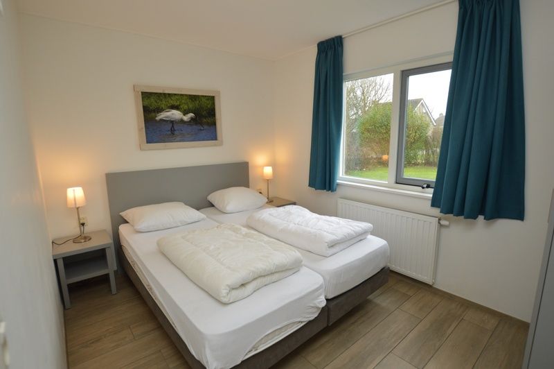 Schlafzimmer im Ferienhaus Stappeland 215, De Koog, Texel, mit bequemen Betten und Blick auf die gruene Umgebung.