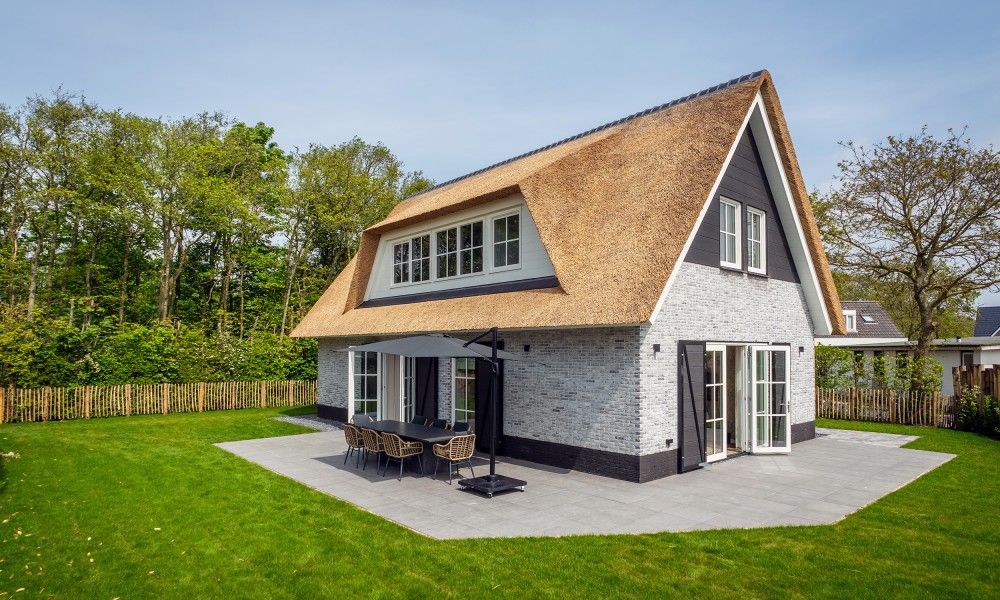 Ferienpark So What in De Koog, Texel: luxurioeses Ferienhaus mit Reetdach und grosser Terrasse, umgeben von gruener Natur.