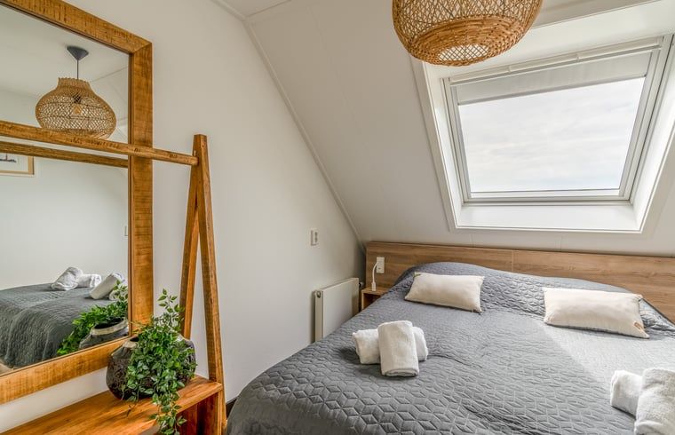 Sfeervolle slaapkamer in Huisje in De Koog, Texel, met dakraam en houten accenten.