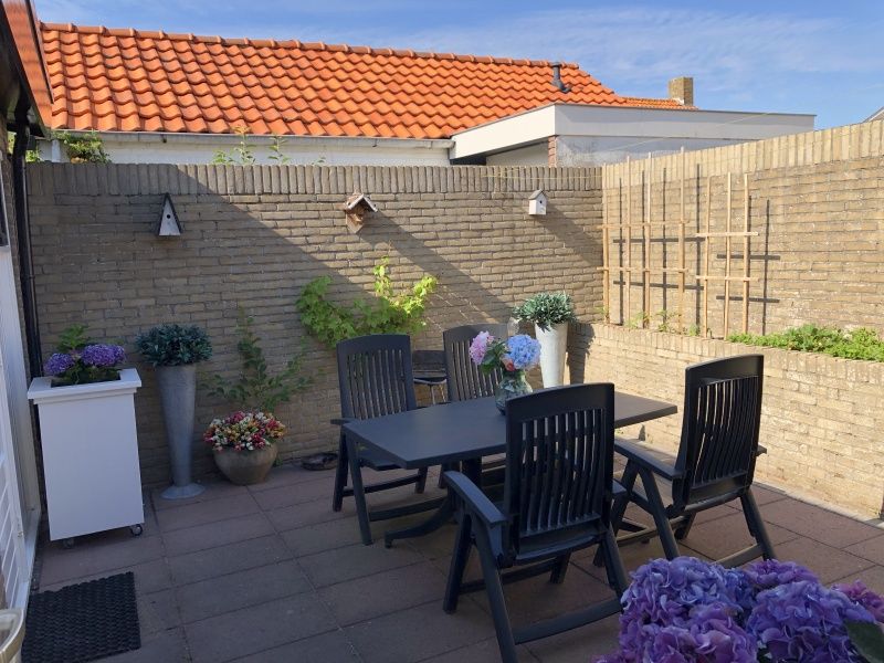 Priveterras van Appartement Duinzee Texel in De Koog, met tuinmeubilair en kleurrijke bloemen.