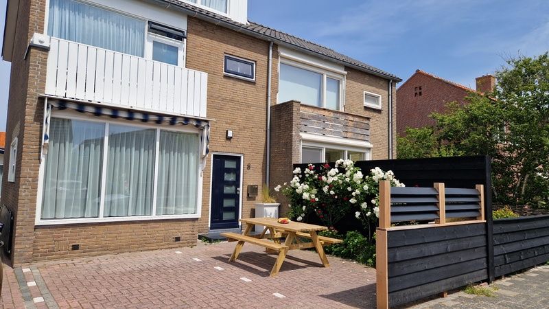 Buitenkant van Vakantiehuis Duinzee Texel in De Koog, met zonnig terras en bloeiende tuin.