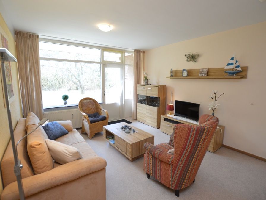 Gemuetliches Wohnzimmer des Appartements Kerckeland 68 in De Koog, Texel mit bequemer Sitzecke und Blick auf die Natur.