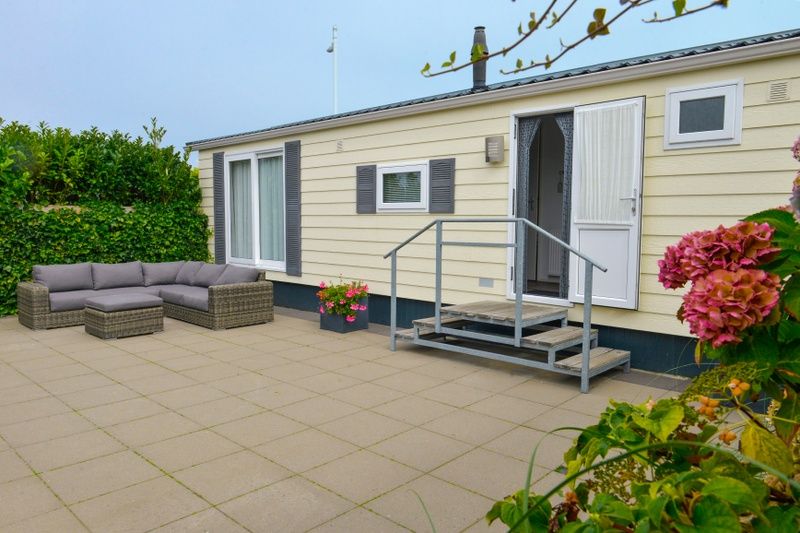 Chalet Bregkoog 138 'Sinne' in De Koog, Texel biedt een ruim terras met loungebank en bloeiende planten.