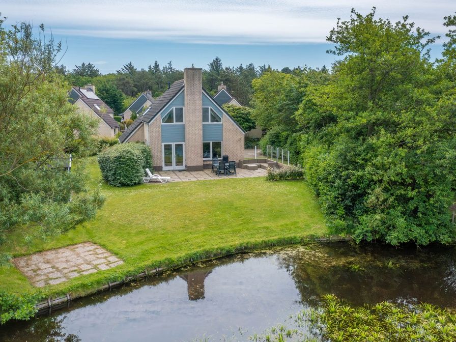 Ferienhaus Honeysuckle 59 in De Koog, Texel, umgeben von ueppiger Natur und einem ruhigen Teich.