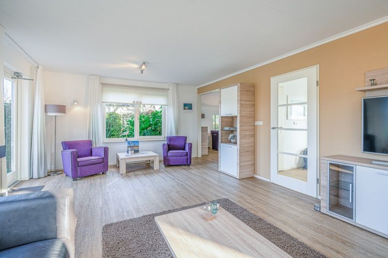 Geraeumiges Wohnzimmer im Ferienhaus Kamperfoelie 59, De Koog, Texel mit lila Sesseln und Gartenblick.