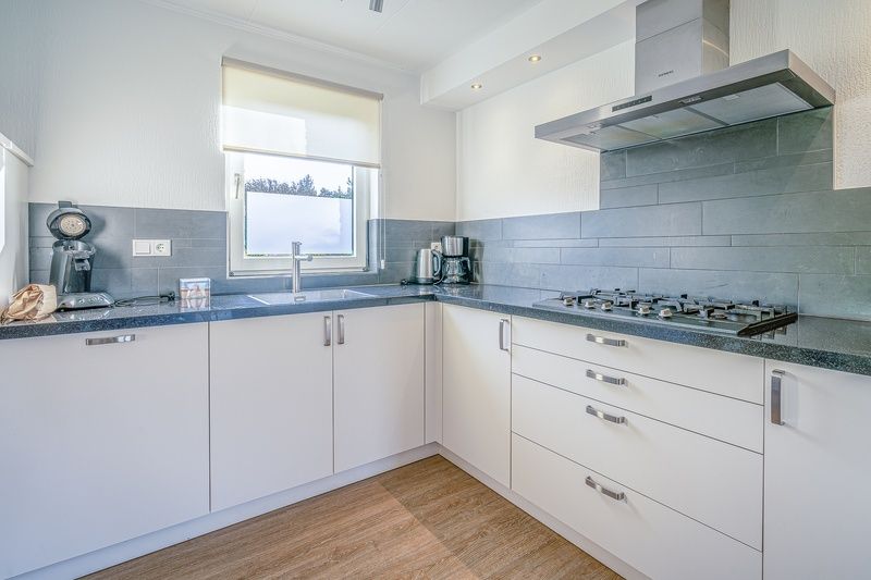 Moderne Kueche im Ferienhaus Kamperfoelie 59, De Koog, Texel mit schlichten weissen Schraenken und Einbaugeraeten.