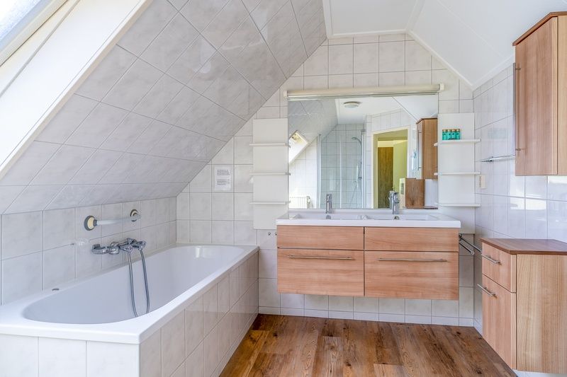 Luxurioeses Badezimmer des Ferienhauses Kamperfoelie 59, De Koog, Texel mit Badewanne, Doppelwaschbecken und moderner Ausstattung.