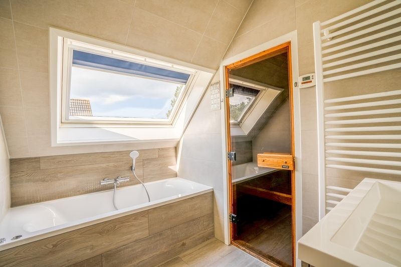 Luxurioeses Badezimmer mit Sauna im Ferienhaus Kamperfoelie 91, De Koog, Texel, ausgestattet mit Badewanne und Dachfenster.
