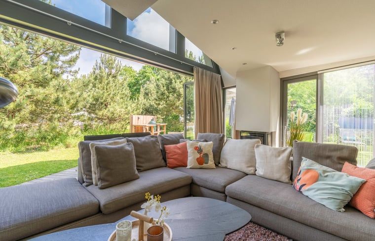 Blick aus dem Wohnzimmer des Ferienhauses in De Koog, Texel, mit gruenem Garten und gemuetlichen Sitzecken, ideal fuer einen ruhigen Urlaub.