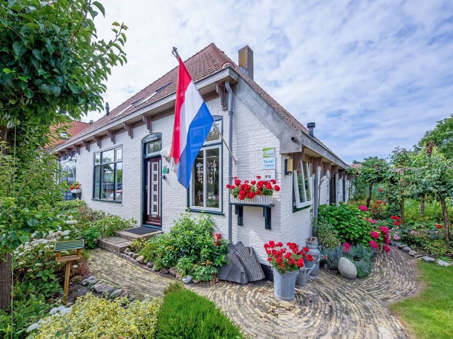 Charmanter Eingang zum Appartement Moleneind in De Waal, Texel, mit buntem Garten und Fahne.