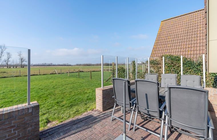 Sunny terrace in Holiday home in De Waal, Texel with comfortable chairs and views of green fields.