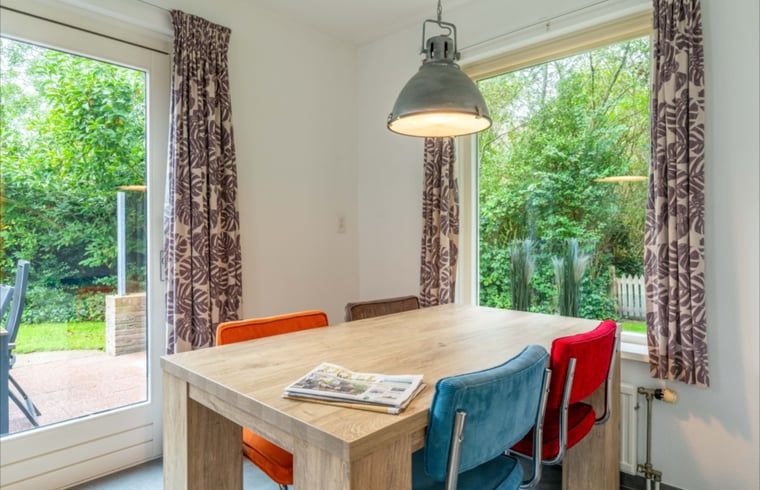 Stijlvolle eetkamer in Huisje in De Waal, Texel met kleurrijke stoelen en uitzicht op de tuin.