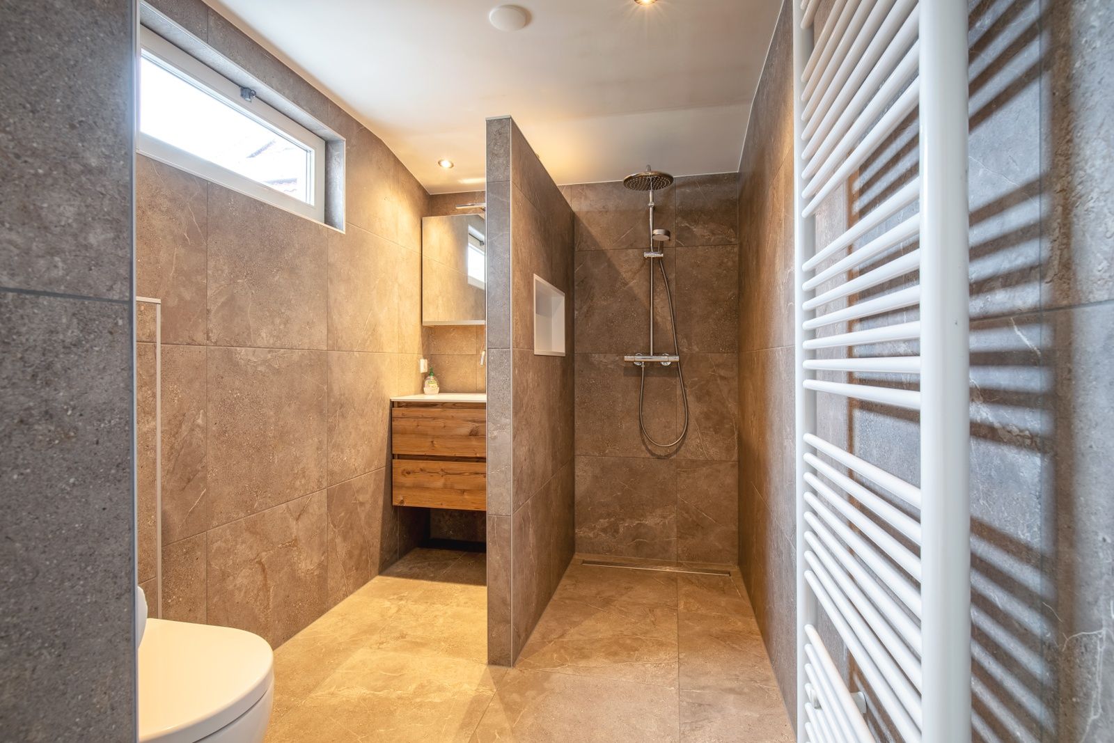 Luxurioeses Badezimmer des Ferienhauses Schoonoord auf Texel mit geraeumiger Dusche und Natursteinfliesen.