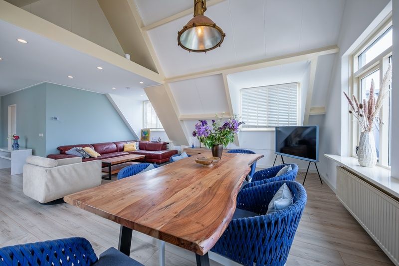 Modernes Wohnzimmer im Hotel Loodsmans Welvaren - Apartment, Den Hoorn, Texel mit geraeumiger Sitzecke und Esstisch aus Holz.