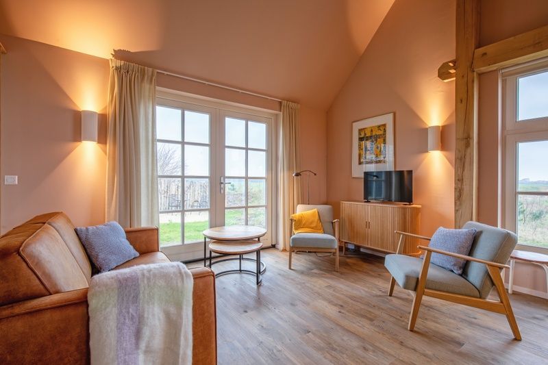 Gemuetliches Wohnzimmer im Ferienhaus Kamille, Den Hoorn, Texel, mit komfortabler Einrichtung und Blick auf die gruene Umgebung.
